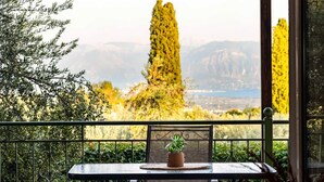 Un balcón con una mesa y sillas, una planta en maceta y vistas a árboles y montañas.