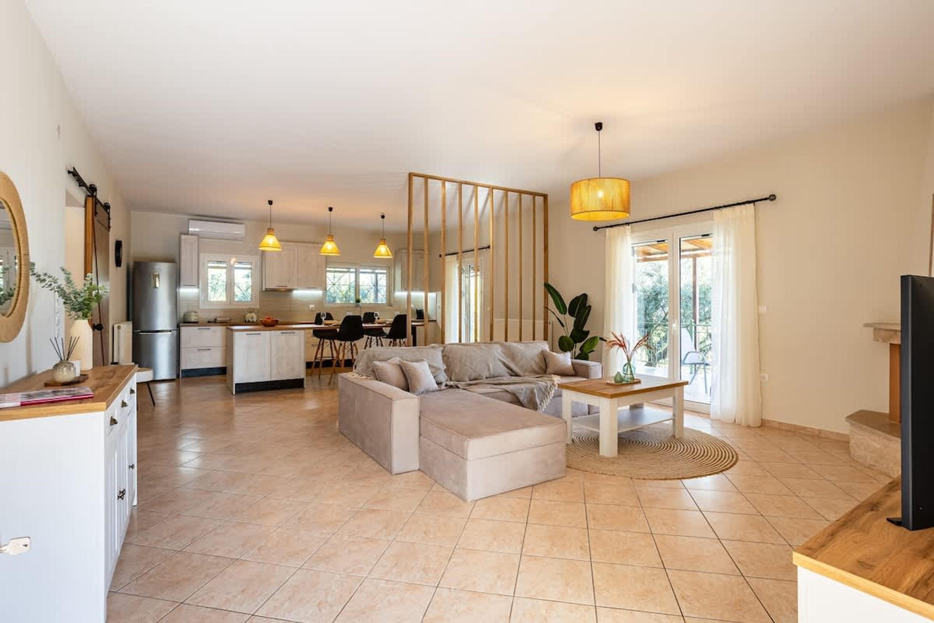 A modern living room with a sofa, coffee table, and pendant lights. A kitchen with cabinets and appliances is visible in the background.