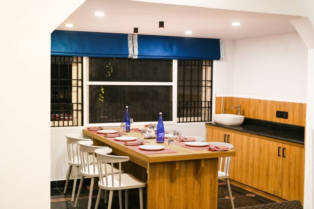 A modern kitchen with a wooden island, white chairs, and a large window with a blue valance.