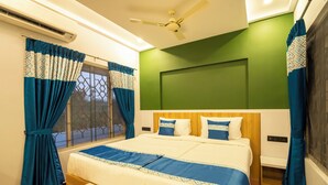A hotel room with a large bed, a ceiling fan, a window with curtains, and a green accent wall.