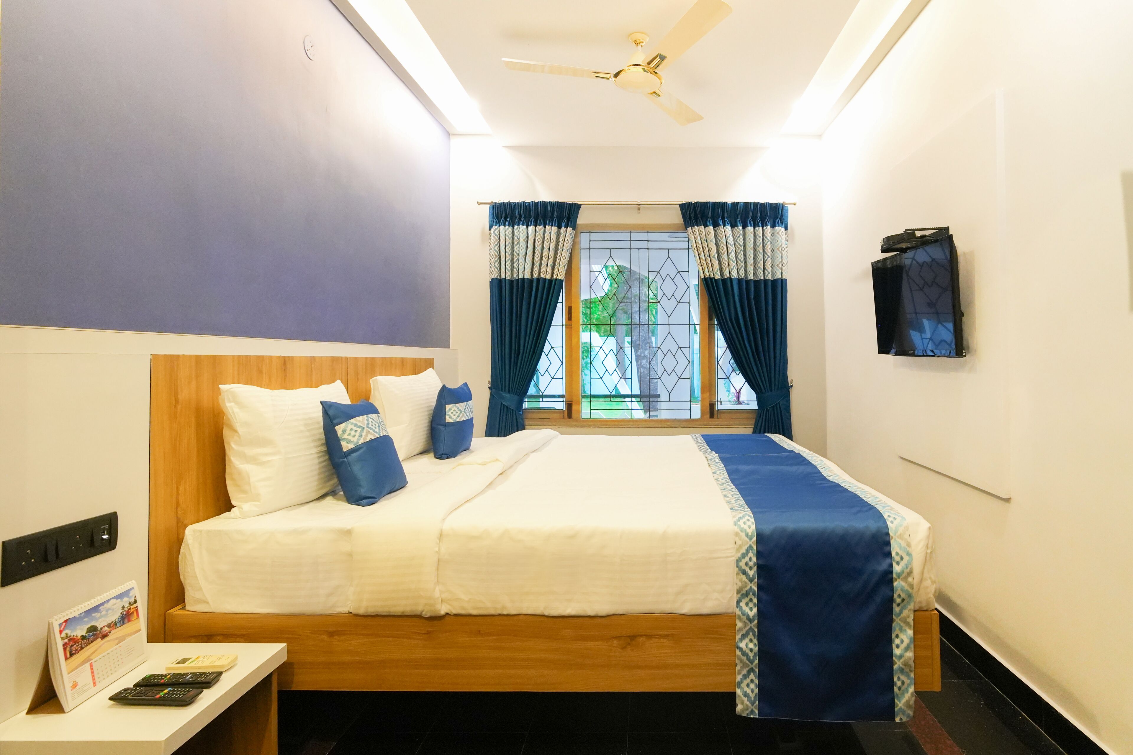 Un dormitorio ordenado con cama, mesita de noche, calendario y ventana con cortinas.