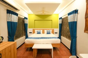 A room with a bed, a small table, a window with curtains, a ceiling fan, and a wall-mounted heater. - MGM Whispering Nest Yelagiri (Tirupattur)