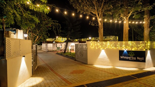 A gated entrance to a property named Whispering Nest, featuring a paved pathway and decorative string lights.