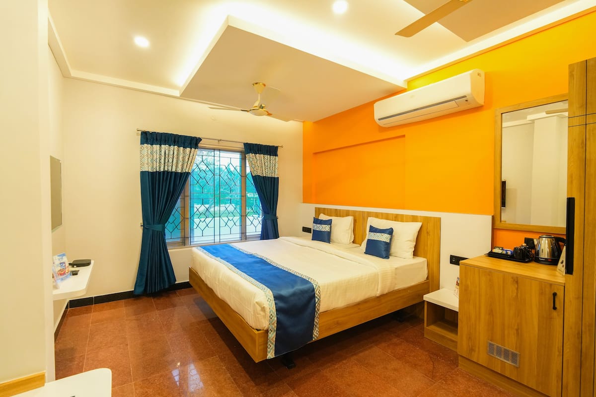 Habitación de hotel con cama, aparador de madera, una mesita y unidad de aire acondicionado.