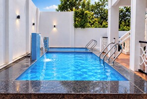 Una piscina rectangular con agua azul cristalina, rodeada de paredes blancas y un suelo de baldosas.
