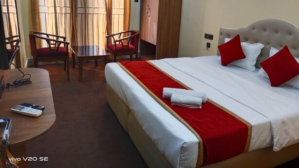 A hotel room with a bed, two chairs, a desk with a calculator, and a wardrobe. - Maa Paradise World (Alipurduar)