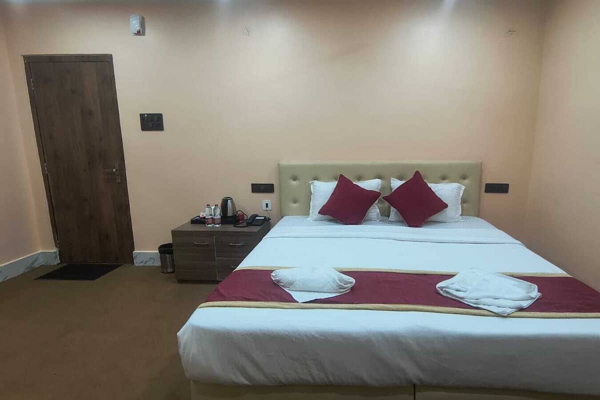 A hotel room with a bed, a nightstand, a wooden door, and a wall socket.