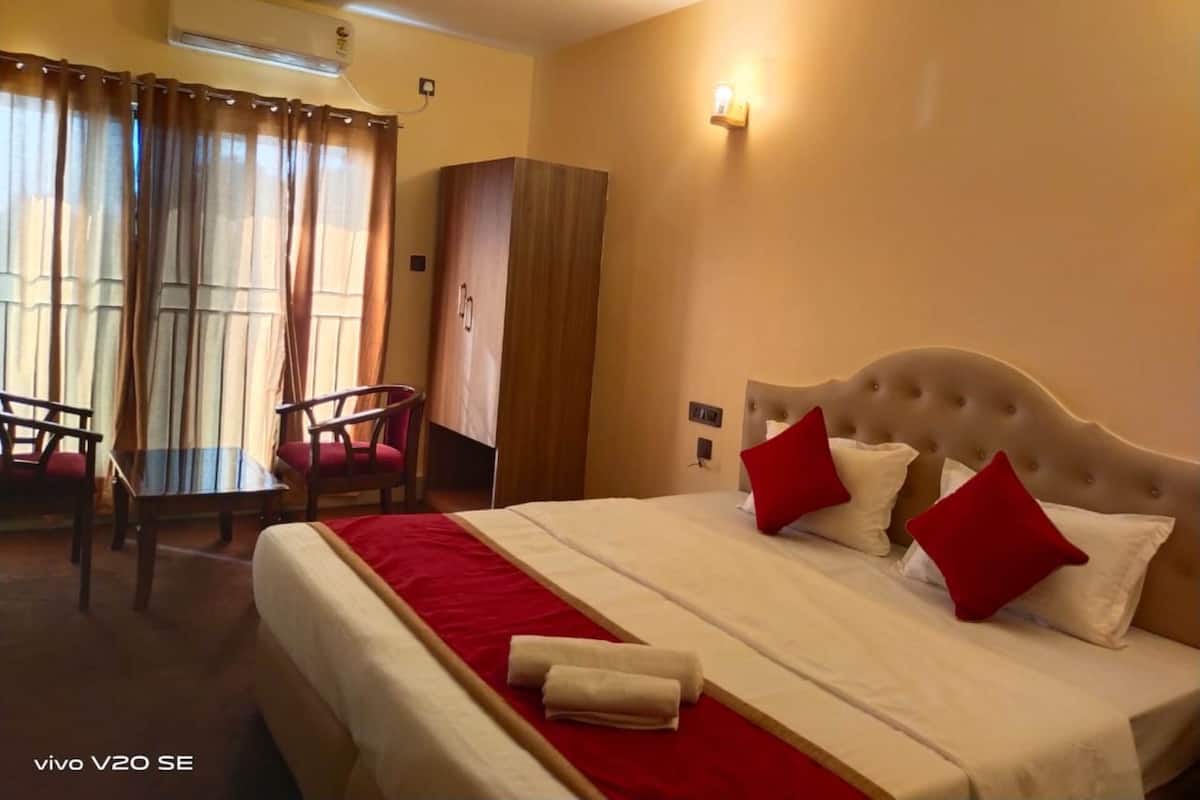 A hotel room with a bed, a desk, and a chair. There is an air conditioning unit on the wall.