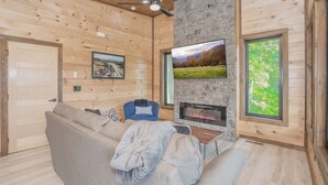 Ein gemütliches Wohnzimmer mit Holzeinrichtung, einem Kamin, einem großen Fernseher und einem bequemen Sofa.