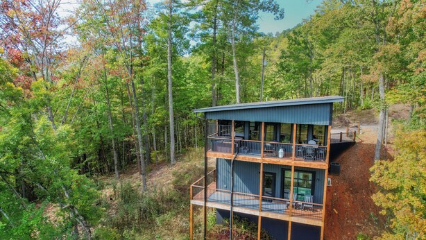 Eine mehrstöckige Hütte mit einem Balkon im oberen Bereich, umgeben von Wald.