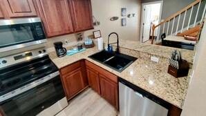 Una cocina moderna con encimeras de granito, electrodomésticos de acero inoxidable, armarios de madera y lavavajillas.