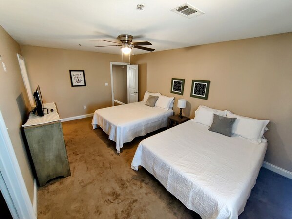 A hotel room with two beds, a ceiling fan, a desk with a computer, and framed pictures on the wall.