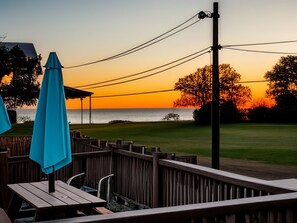 A wooden deck with a table and chairs, overlooking a body of water during sunset.
