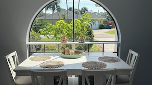 A dining area with a large window, white table, and chairs, featuring a view of a residential neighborhood. - Coastal Getaway with game room pool hot tub & inlaw suite in heart of Sebastian (Sebastian)