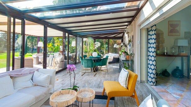 A sunlit patio with a glass enclosure, a dining area with green chairs, a yellow armchair, and wicker side tables. - Beautiful home in Graveson (Graveson)