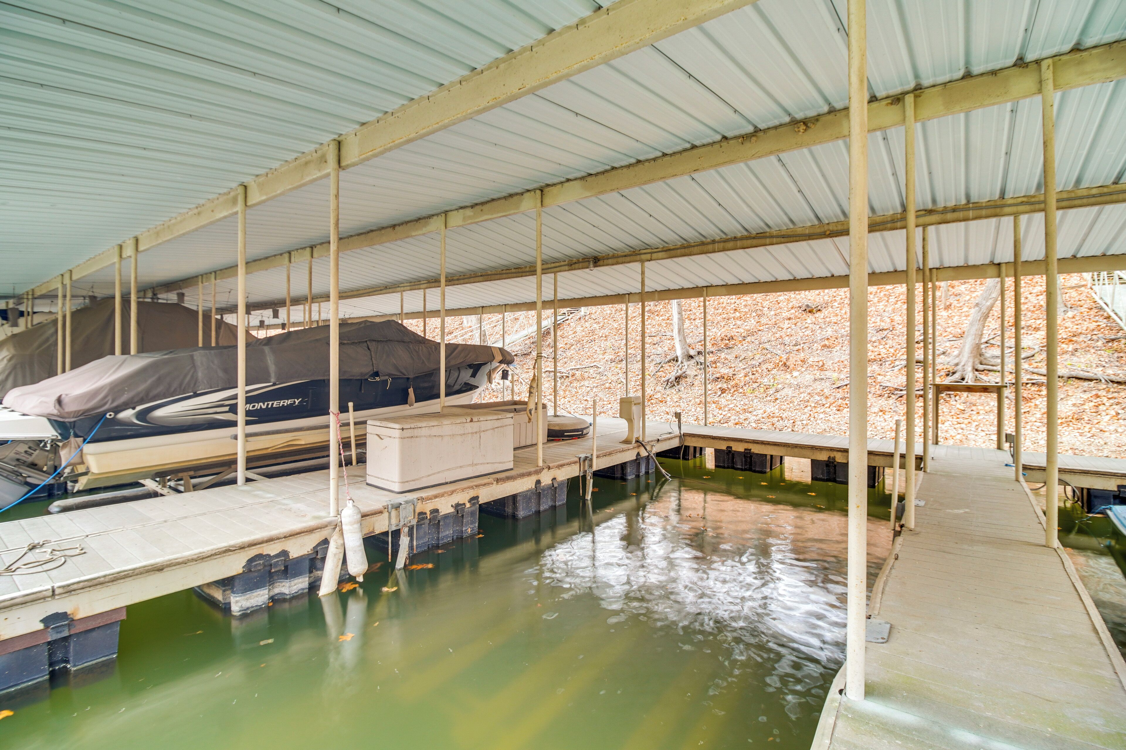 Un quai abrité avec un bateau recouvert d’une bâche, un hangar à bateaux en béton et un quai s’étendant dans une étendue d’eau.