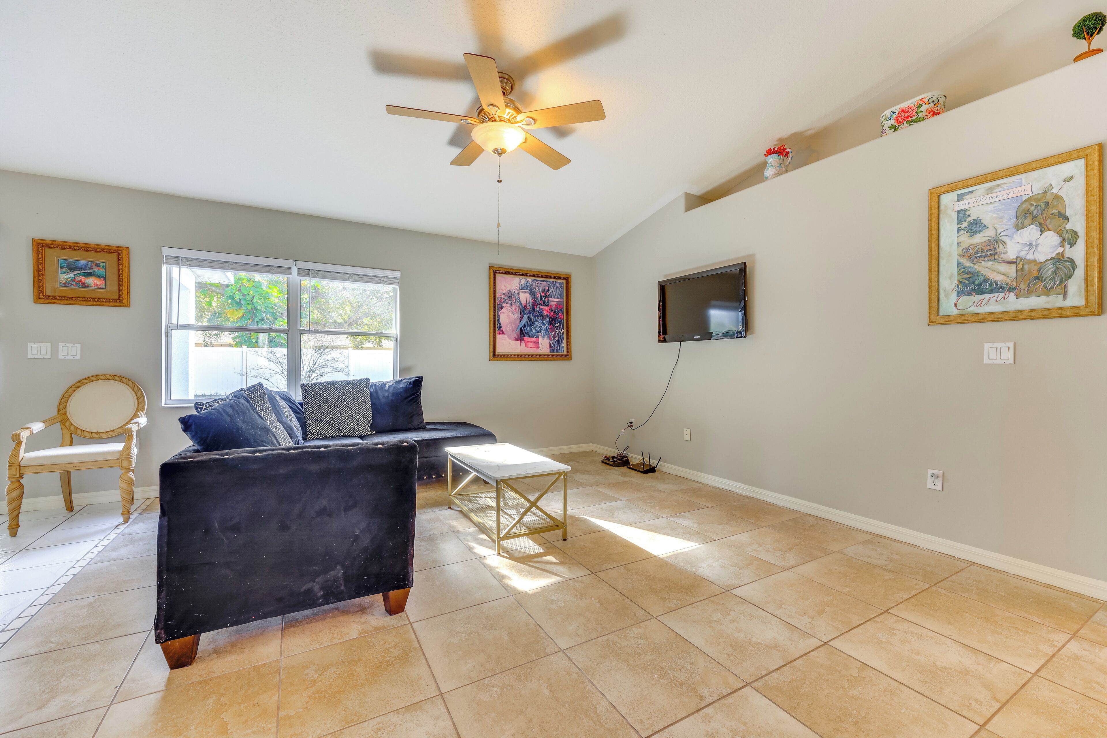 A spacious living room with a ceiling fan, a black sofa, a wooden coffee table, and a large window providing natural light.