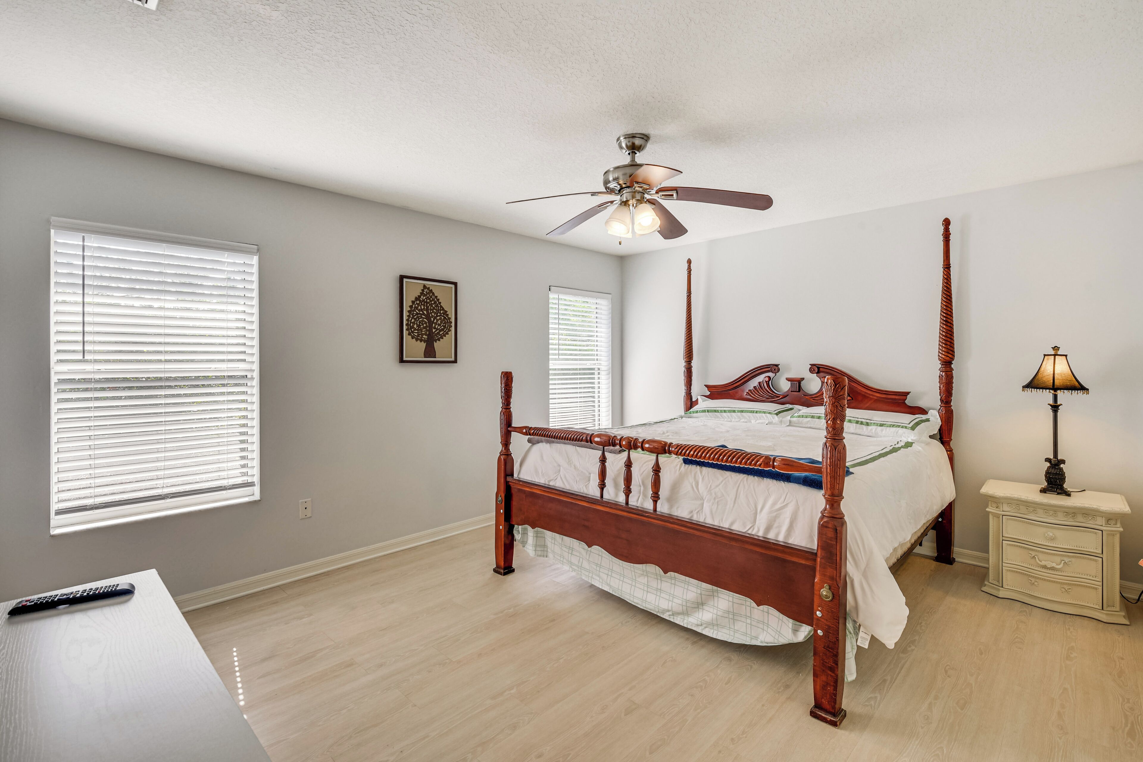 A bedroom with a four-poster bed, a ceiling fan, and a nightstand with a lamp.