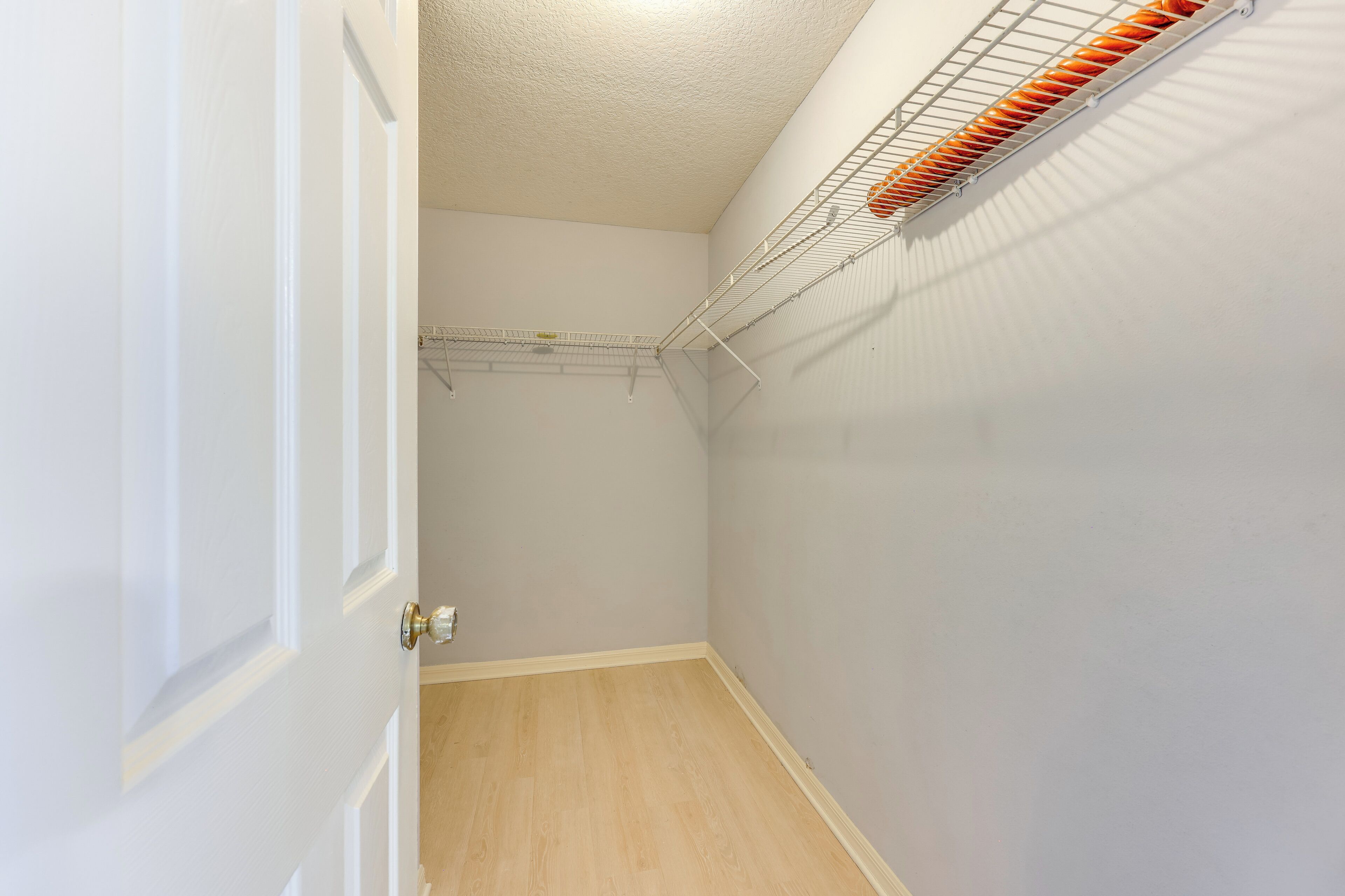 Um corredor estreito com uma porta branca, piso de madeira e uma prateleira no teto com objetos laranja.