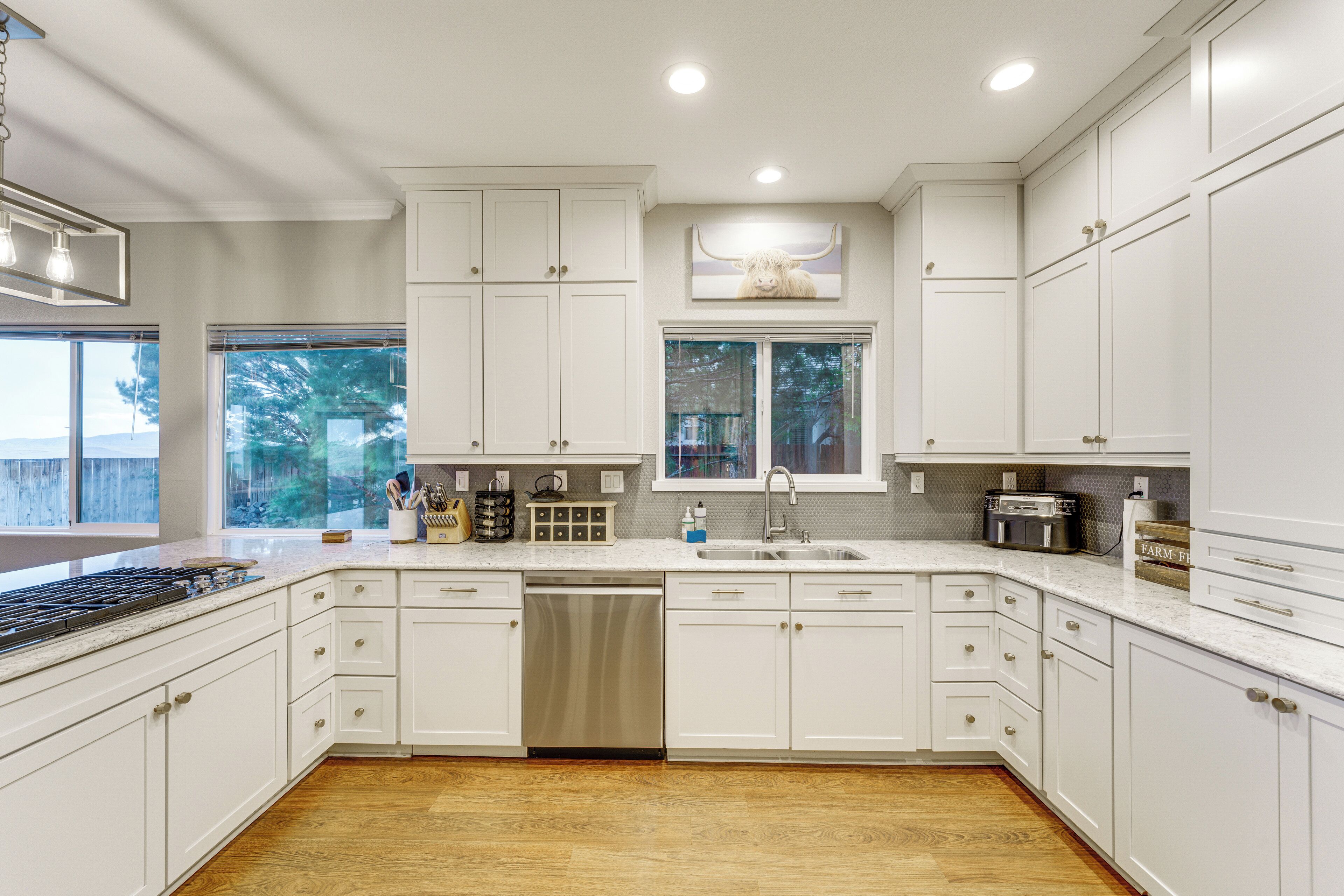 A kitchen with white cabinets, a dishwasher, a stove, and a window with a view of trees.