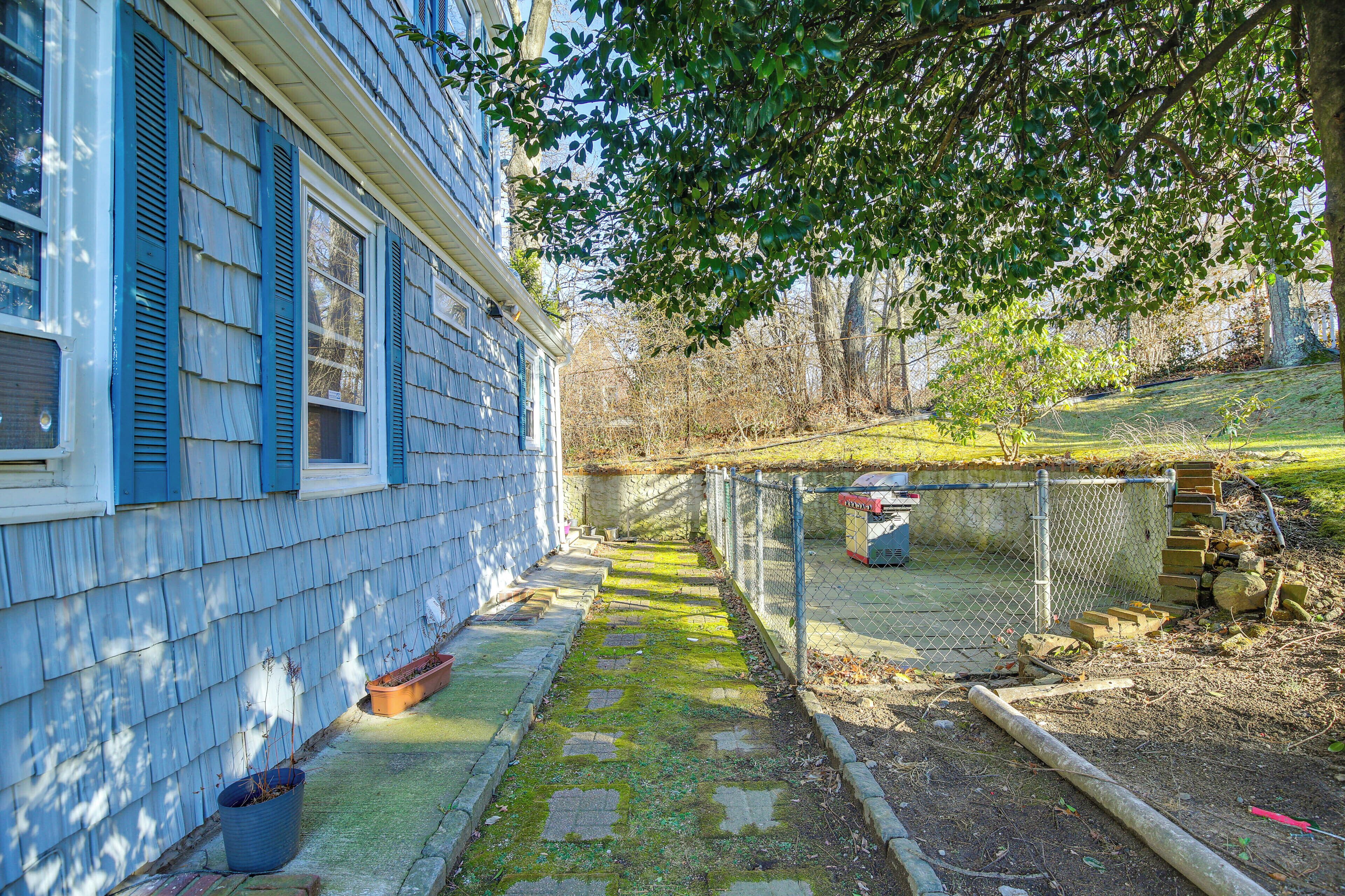 A residential property with a stone pathway leading to a fenced yard, a blue house with shutters, and a tree providing shade.