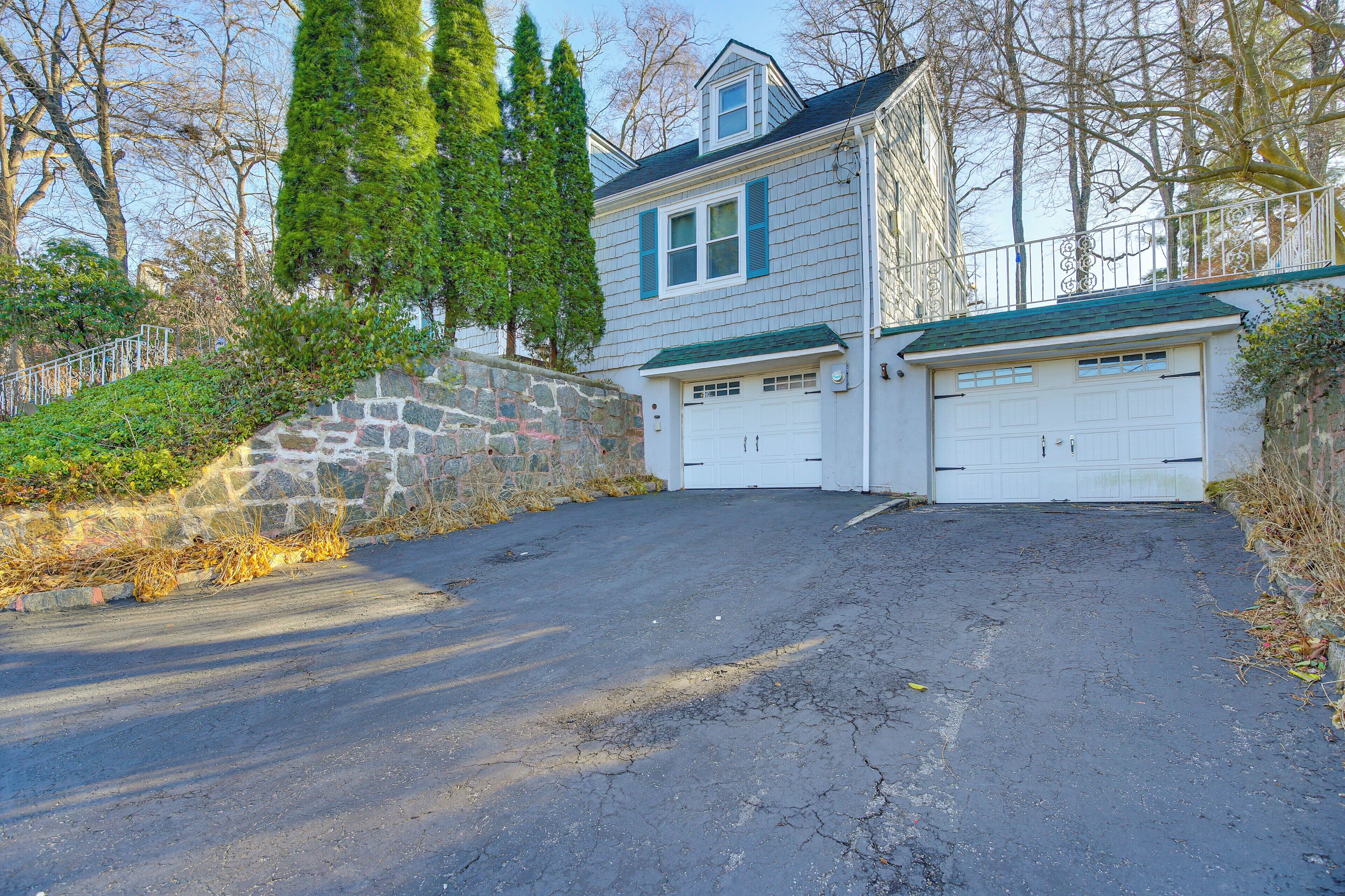 A two-story house with a stone retaining wall, a garage, and a driveway leading to the garage.
