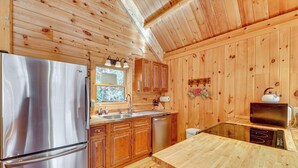 Cocina de cabaña de madera con un refrigerador de acero inoxidable, armarios de madera, un lavamanos y un microondas.
