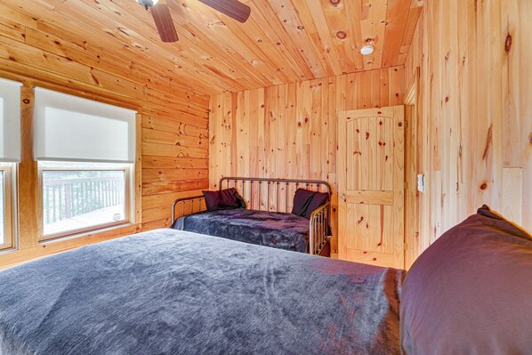 A wooden cabin room with two beds, a window, and a door.