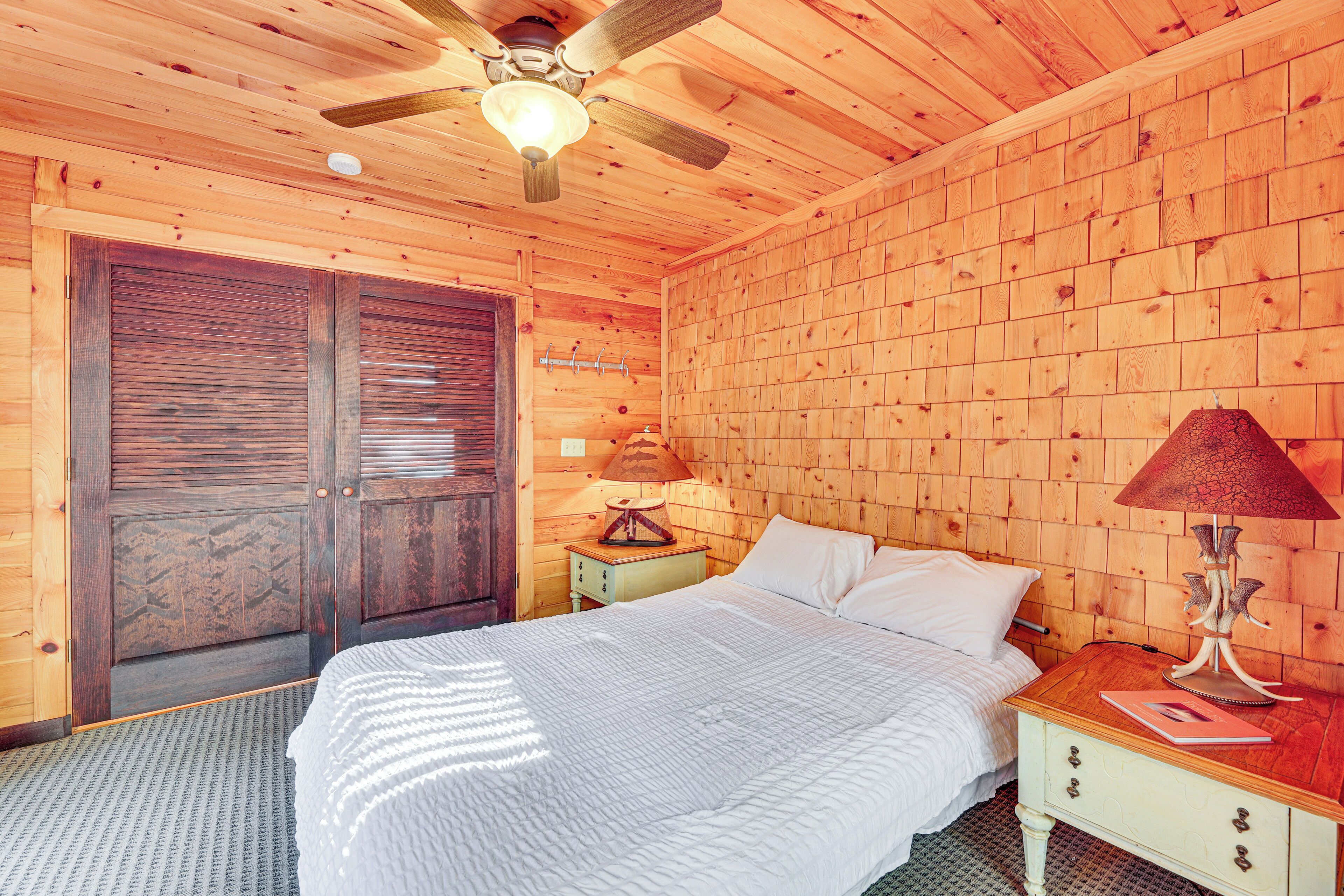 A wooden-paneled room with a bed, a nightstand, a lamp, and a ceiling fan.