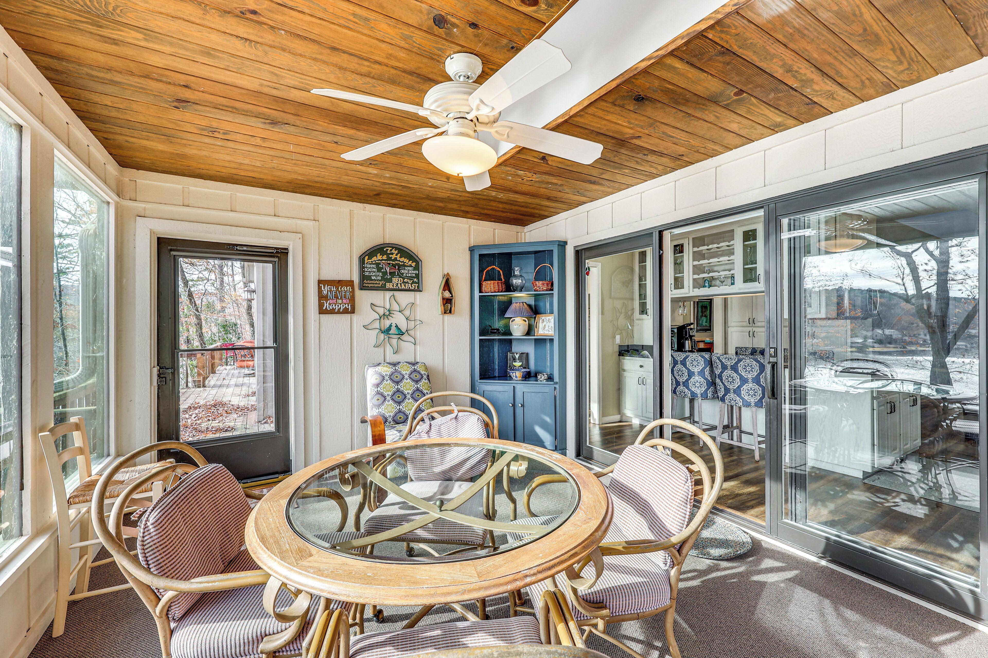 A cozy room with a wooden ceiling, a ceiling fan, a round glass table, wicker chairs, and a blue cabinet with decorative items.