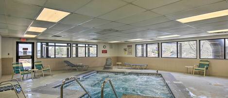 Et indendørs pool med klart vand, omgivet af liggestole og et flisegulv.
