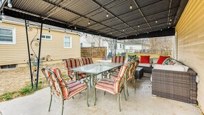 An outdoor patio with a glass-top table surrounded by striped chairs, a wicker sofa with red cushions, and a metal pergola overhead. - Dog-friendly Home w/ Patio & Yard in Greeley (Greeley)