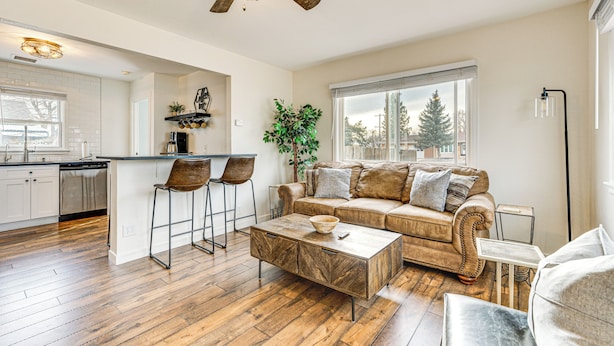 A spacious living area with a wooden floor, a brown leather sofa, a coffee table, and a ceiling fan. - Dog-friendly Home w/ Patio & Yard in Greeley (Greeley)