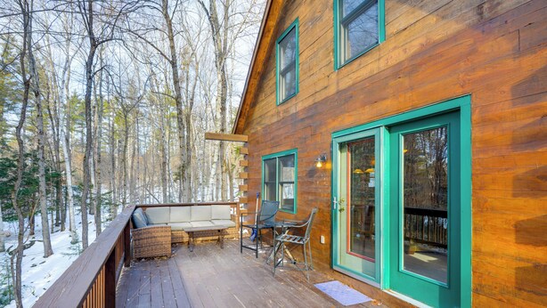 Une cabane en bois dotée d’une terrasse, d’un banc et de deux chaises.