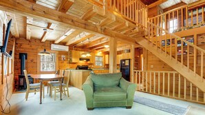 L’intérieur d’un chalet en bois comprend un coin repas, un canapé vert et un escalier menant à un niveau supérieur.