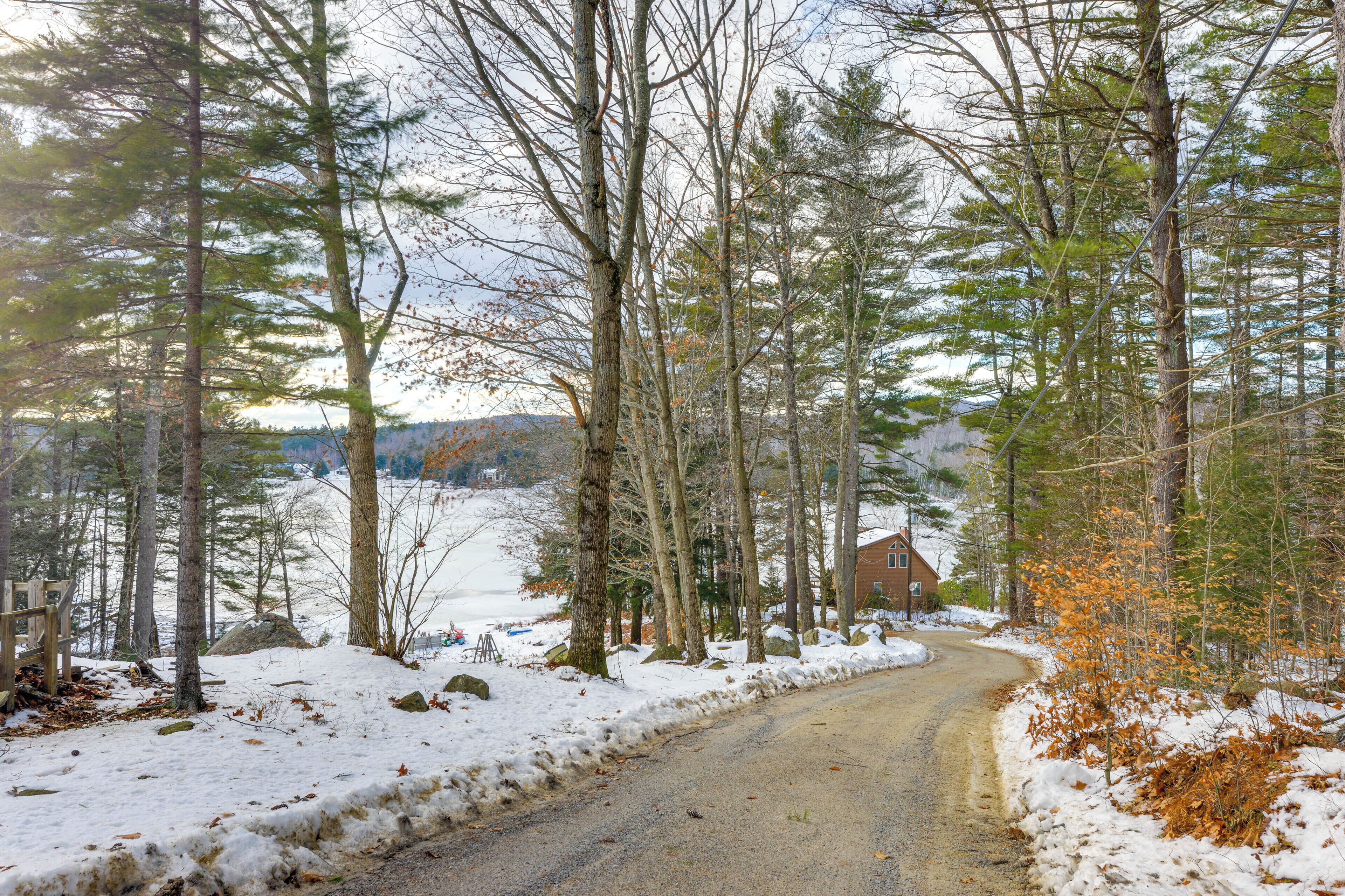 A snow-covered rural road flanked by tall trees and a distant house.