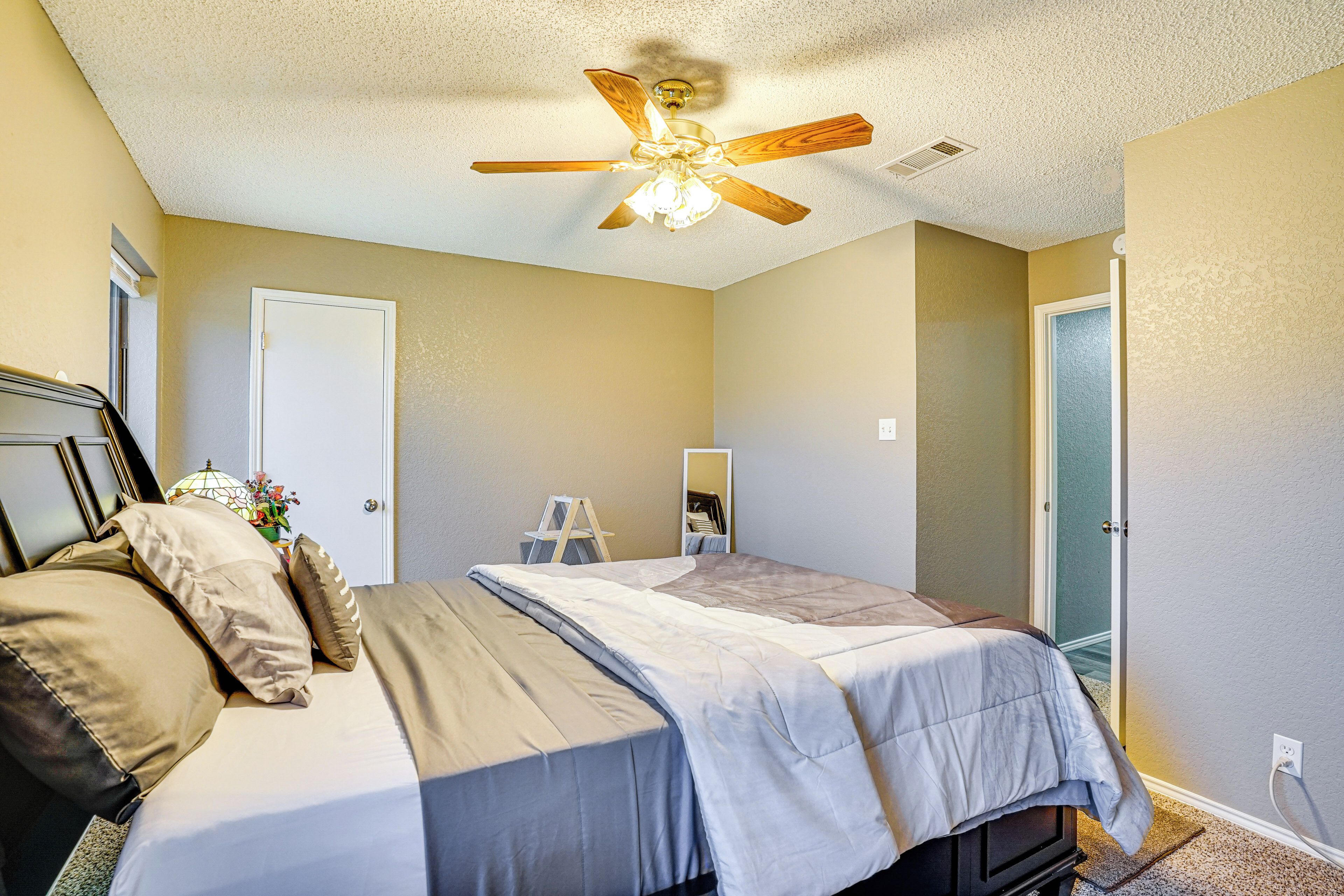 A bedroom with a bed, a ceiling fan, a dresser, and a door.