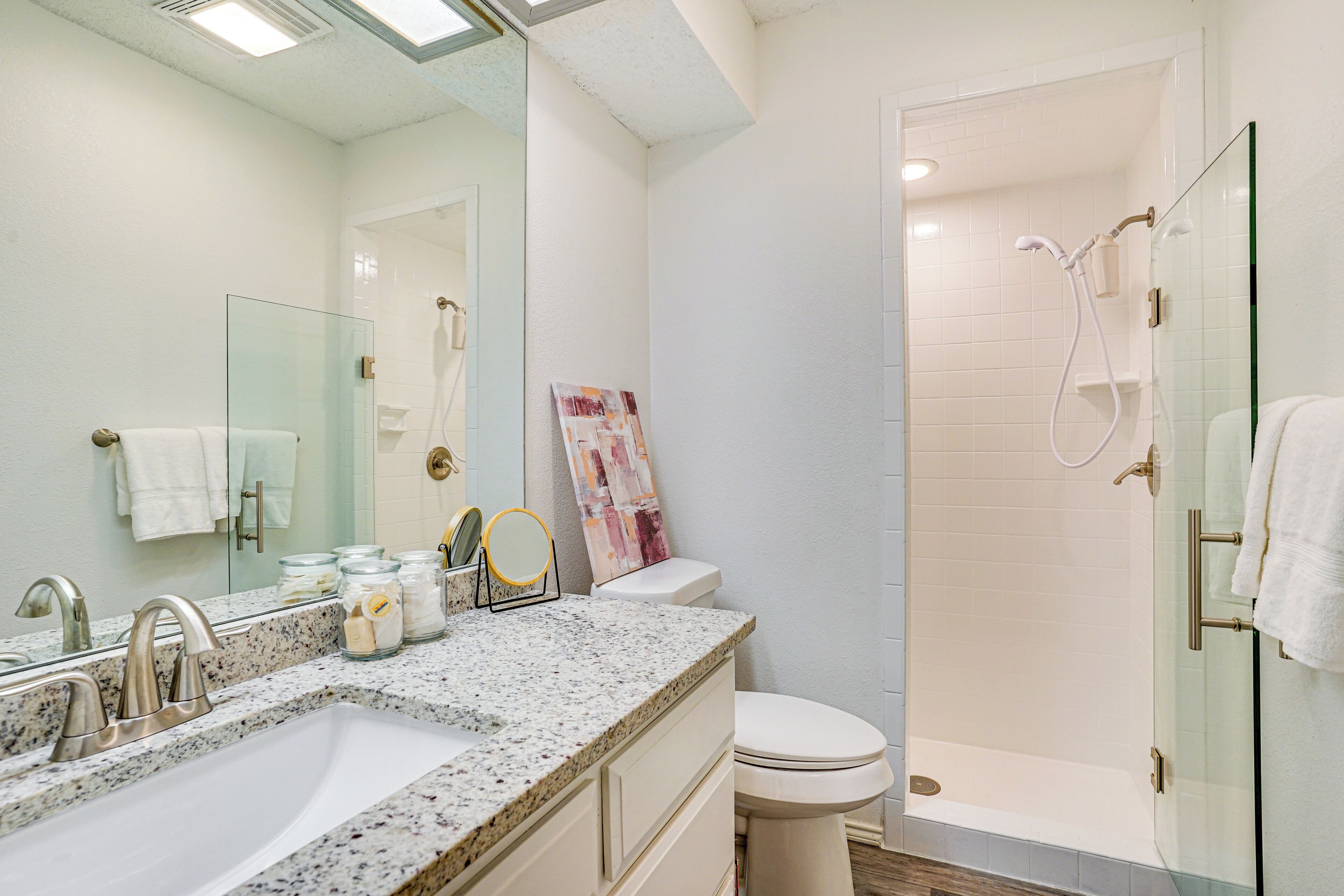 A bathroom with a granite countertop sink, a toilet, and a glass-enclosed shower.