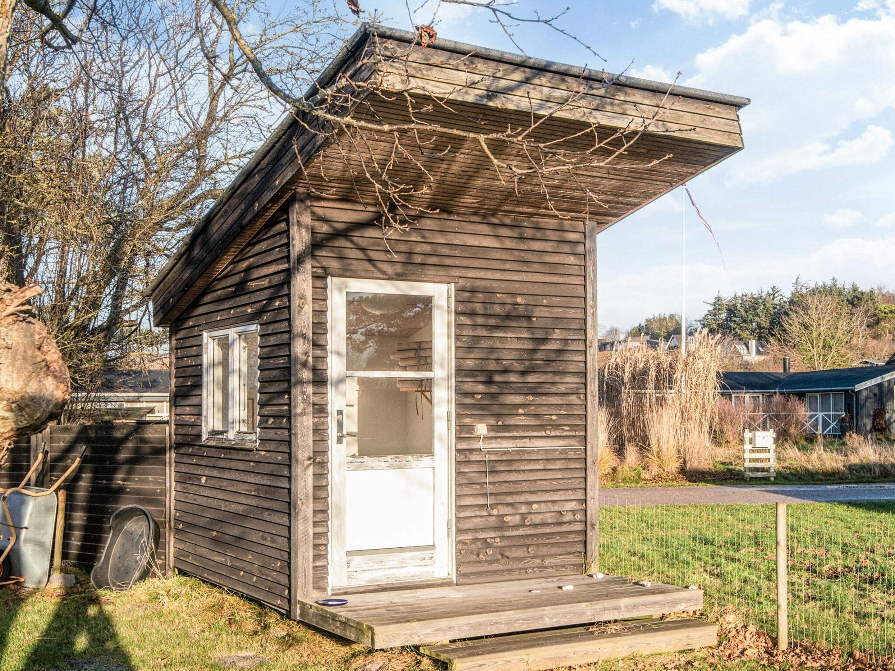 A small wooden cabin with a door and windows, situated in a grassy area with trees in the background.
