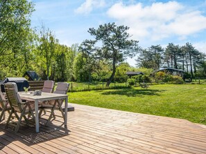 An outdoor deck with a table and chairs, surrounded by a grassy area and trees. - 4 Person Holiday Home in Knebel (Knebel)