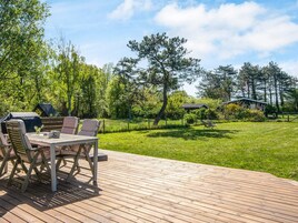 Una terraza al aire libre con una mesa y sillas, rodeada de césped y árboles.