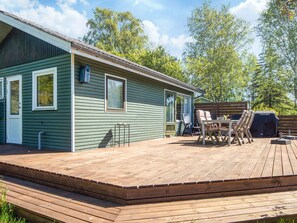 A green house with a wooden deck, a table, chairs, and a barbecue grill. - 4 Person Holiday Home in Knebel (Knebel)
