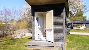 A small wooden structure with a door open, revealing a white interior with a bed and a small table.