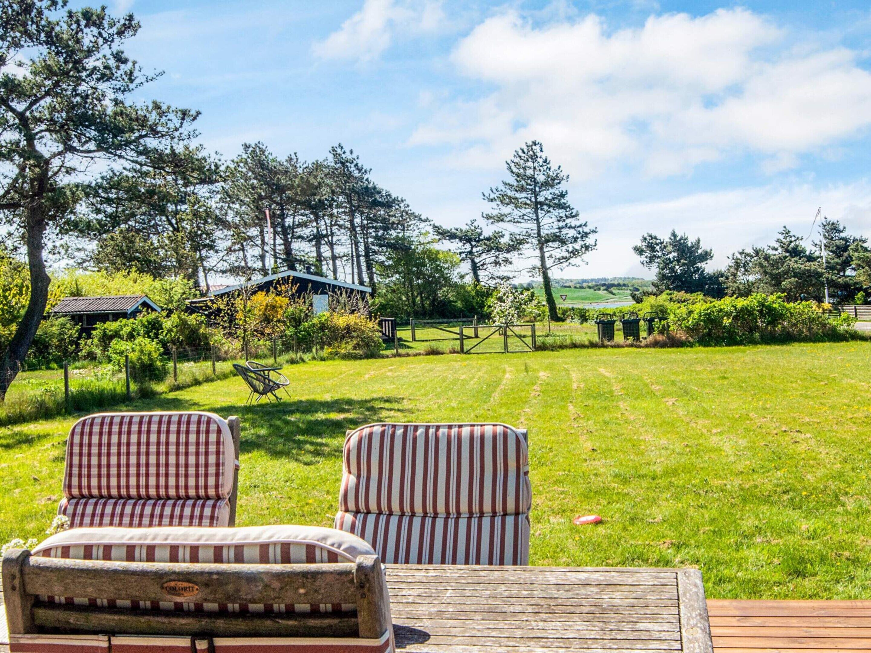 A wooden deck with two striped chairs facing a grassy lawn and a house in the background.