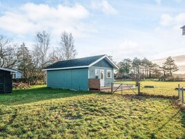 A small, single-story building with a green exterior and a sloped roof, surrounded by a grassy yard and trees.