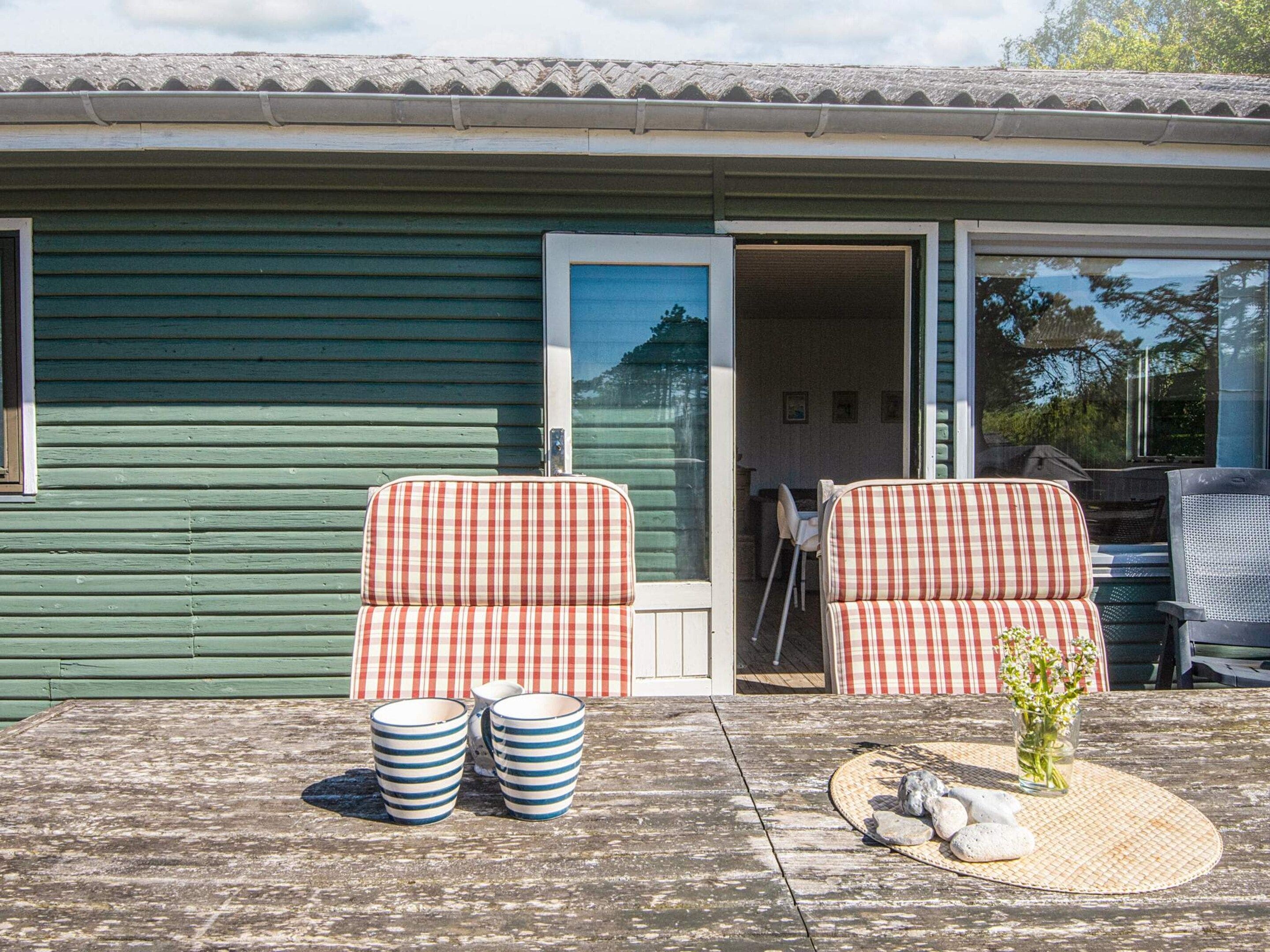 Une terrasse avec deux canapés à motifs à carreaux, une table ornée d’un vase de fleurs et une paire de tasses rayées.