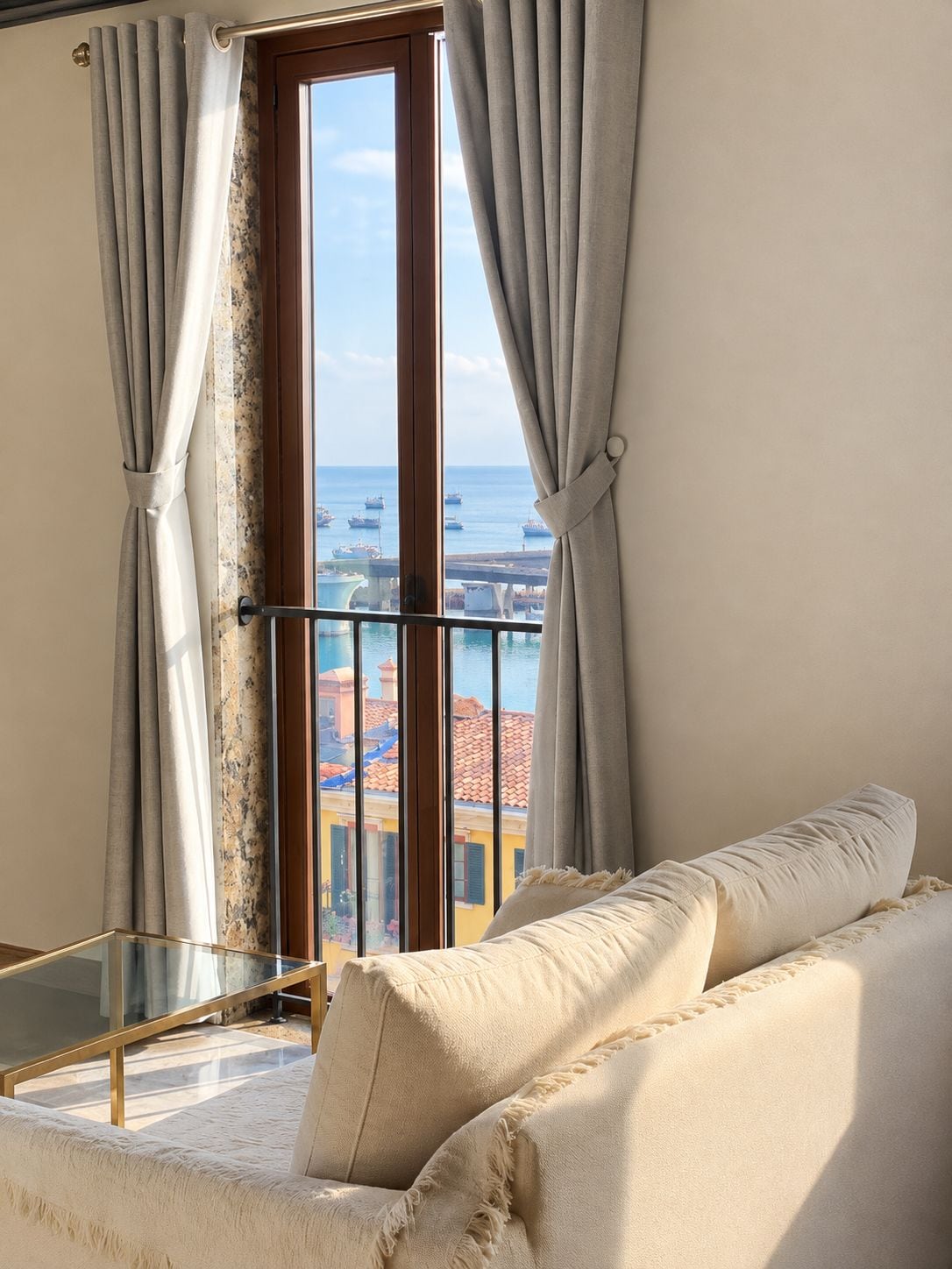 Ein Zimmer mit Balkon, einer Couch und Blick auf das Meer und Gebäude.