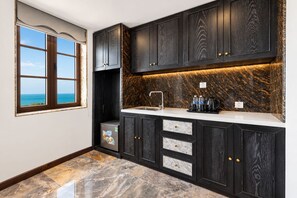 A modern kitchen with dark wood cabinets, a marble countertop, and a view of the ocean through a window. - The Nice Hotel Phu Quoc - Fireworks & Ocean view (Phu Quoc)