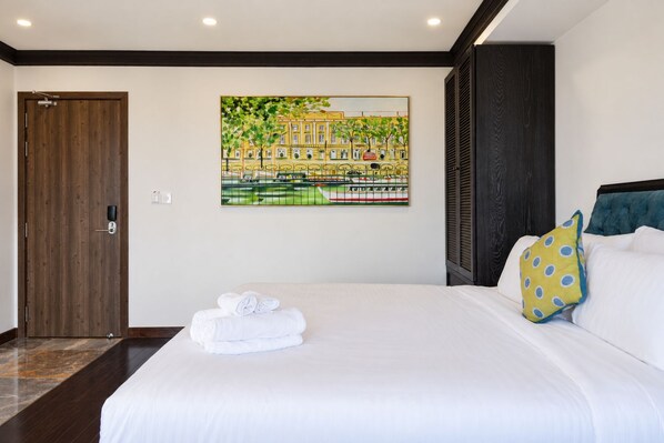A hotel room with a large bed, a painting of a cityscape, a wooden door, and a dark-colored headboard.