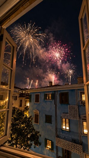 A view through a window of a building with multiple windows and balconies, with fireworks in the sky. - The Nice Hotel Phu Quoc - Fireworks & Ocean view (Phu Quoc)